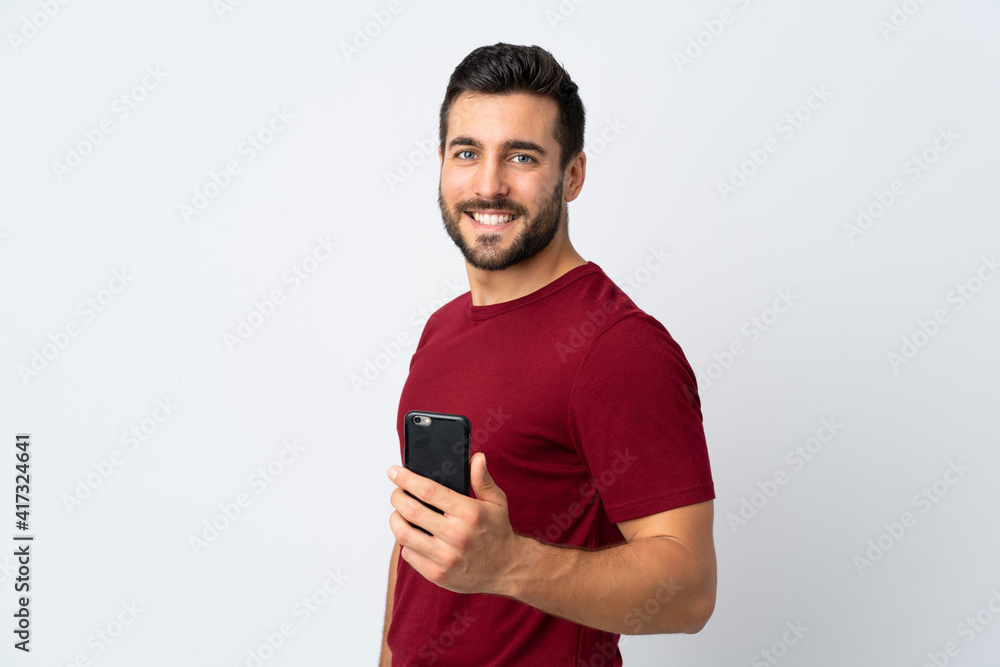 Young handsome man with beard using mobile phone isolated on white background smiling a lot Young handsome man with beard using mobile phone isolated on white background smiling a lot