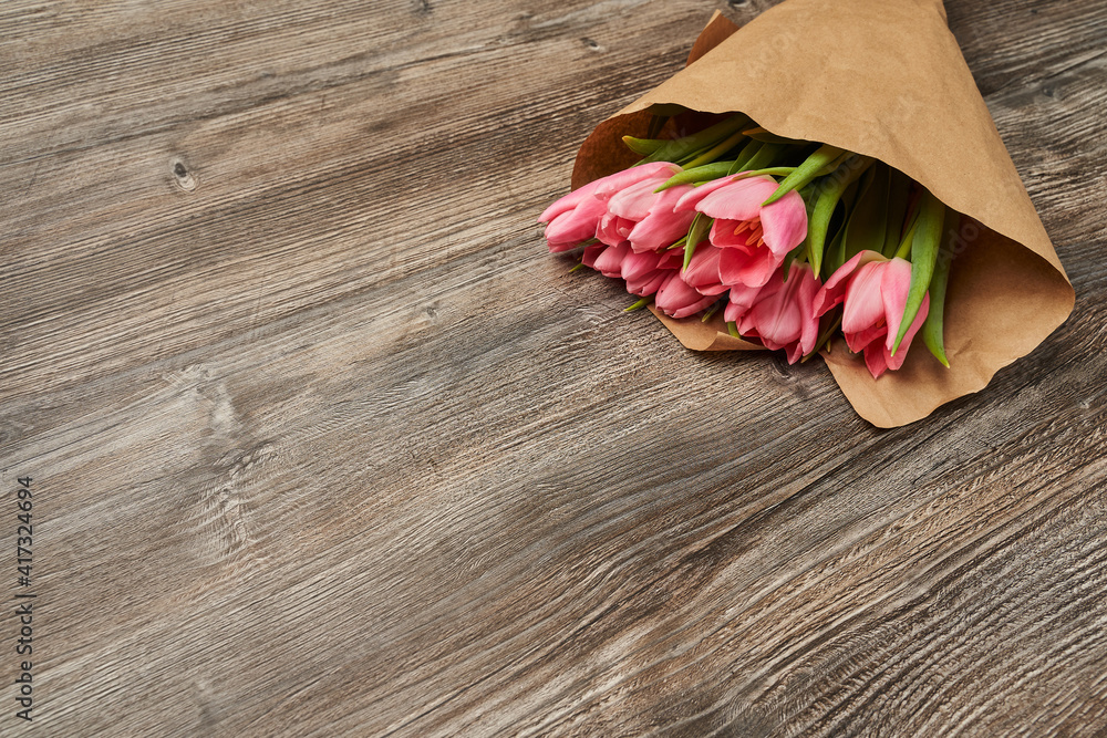 a bouquet of several pink tulips lies beautifully in craft paper on a wooden background in the upper left corner a bouquet of several pink tulips lies beautifully in craft paper on a wooden background in the upper left corner