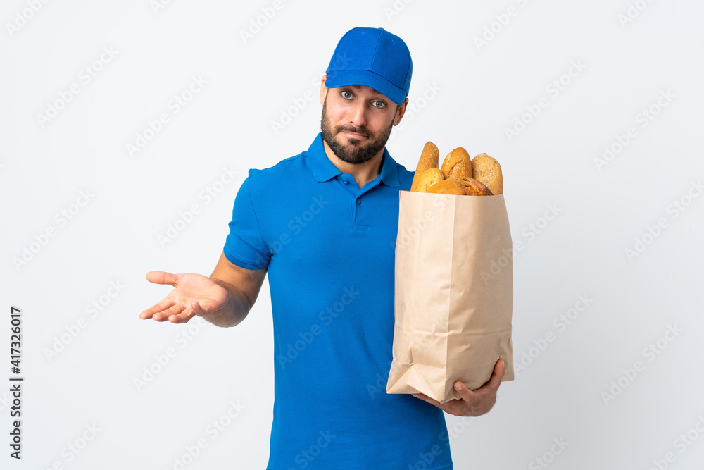 Delivery man holding a bag full of breads isolated on white background making doubts gesture while lifting the shoulders Delivery man holding a bag full of breads isolated on white background making doubts gesture while lifting the shoulders