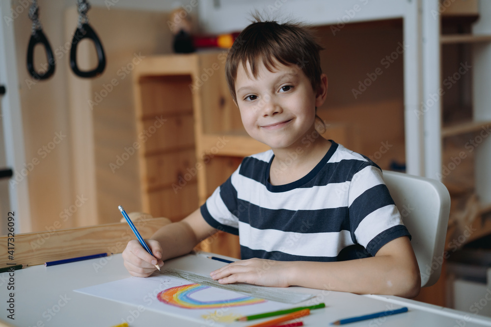 adorable caucasian boy of elementary age drawing with pencils sitting at the desk in his room at home. Image with selective focus adorable caucasian boy of elementary age drawing with pencils sitting at the desk in his room at home. Image with selective focus