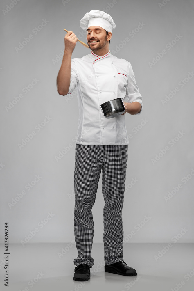 cooking, culinary and people concept - happy smiling male chef in toque with pot or saucepan and spoon tasting food over grey background cooking, culinary and people concept - happy smiling male chef in toque with pot or saucepan and spoon tasting food over grey background