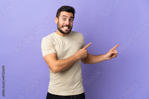 Young handsome man with beard over isolated background frightened and pointing to the side