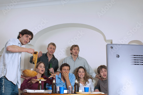 Amici guardano la partita a casa mentre bevono e mangiano gli spaghetti photo