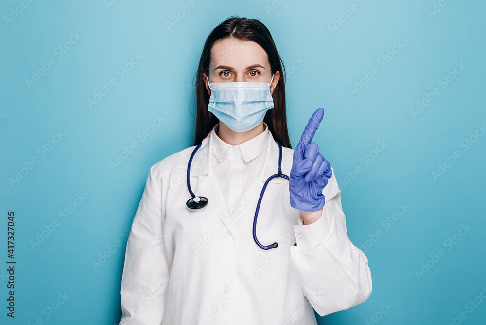 Serious professional woman doctor in protective face mask and gloves warning people, shaking finger in prohibition restriction, isolated on blue wall. Medical workers, pandemic coronavirus concept Serious professional woman doctor in protective face mask and gloves warning people, shaking finger in prohibition restriction, isolated on blue wall. Medical workers, pandemic coronavirus concept