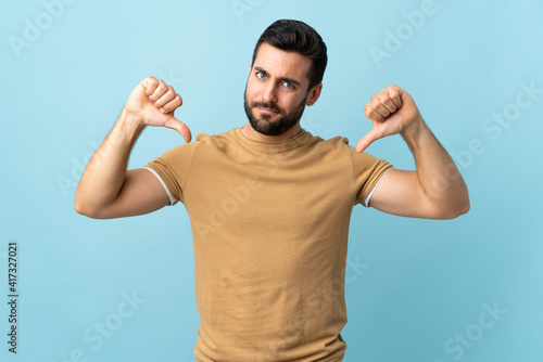 Young handsome man with beard over isolated background showing thumb down with two hands