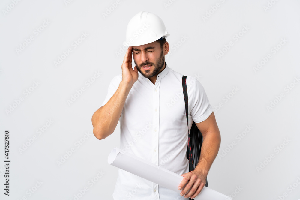 Young architect man with helmet and holding blueprints isolated on white background with headache Young architect man with helmet and holding blueprints isolated on white background with headache