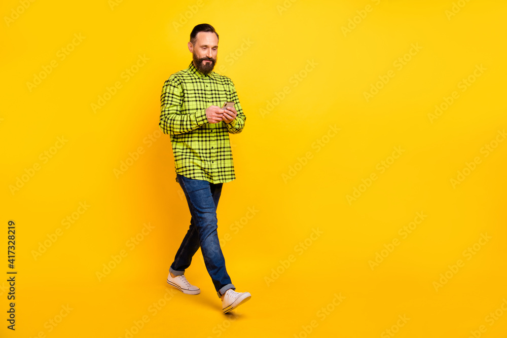 Full size profiles die photo of handsome man happy smile go walk look read browse cellphone isolated over yellow color background Full size profiles die photo of handsome man happy smile go walk look read browse cellphone isolated over yellow color background