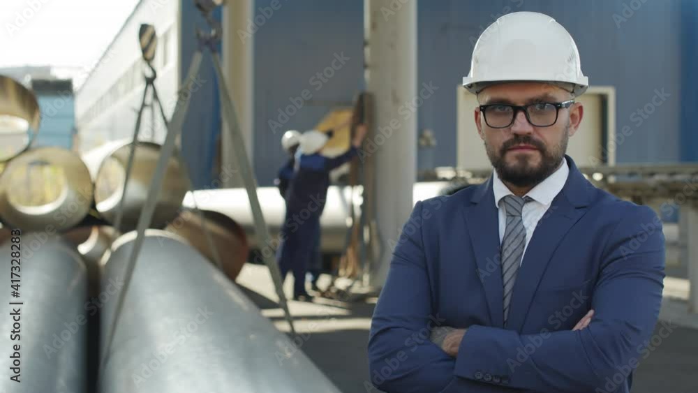 PAN portrait shot of male engineer in suit and hard hat posing for camera outdoors in industrial setting PAN portrait shot of male engineer in suit and hard hat posing for camera outdoors in industrial setting