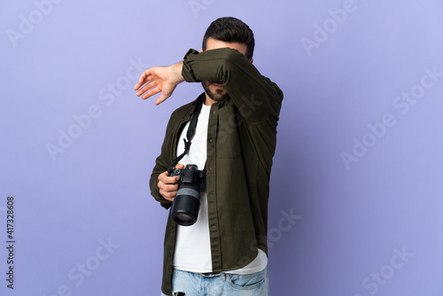 Photographer man over isolated purple background covering eyes by hands