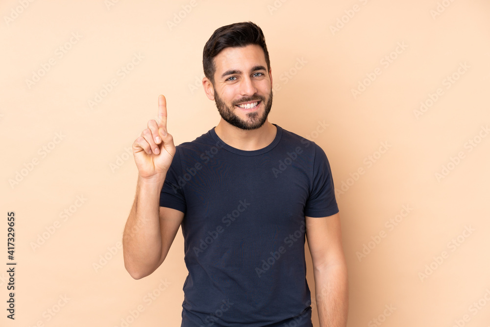 Caucasian handsome man isolated on beige background showing and lifting a finger in sign of the best Caucasian handsome man isolated on beige background showing and lifting a finger in sign of the best