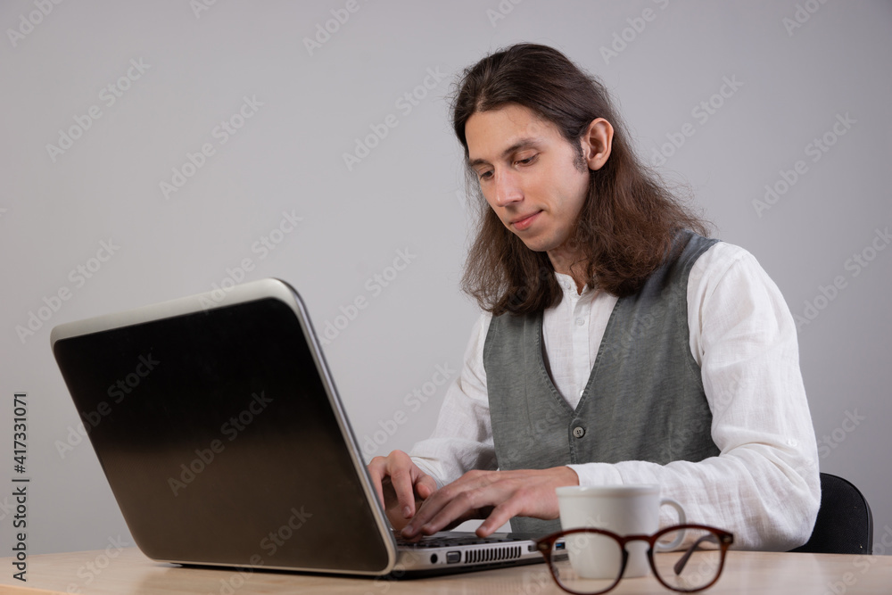 geek guy is learning new technologies, programming, and computer modeling. The student studies programming languages, e-learning. A young man with long hair is working on a laptop. geek guy is learning new technologies, programming, and computer modeling. The student studies programming languages, e-learning. A young man with long hair is working on a laptop.