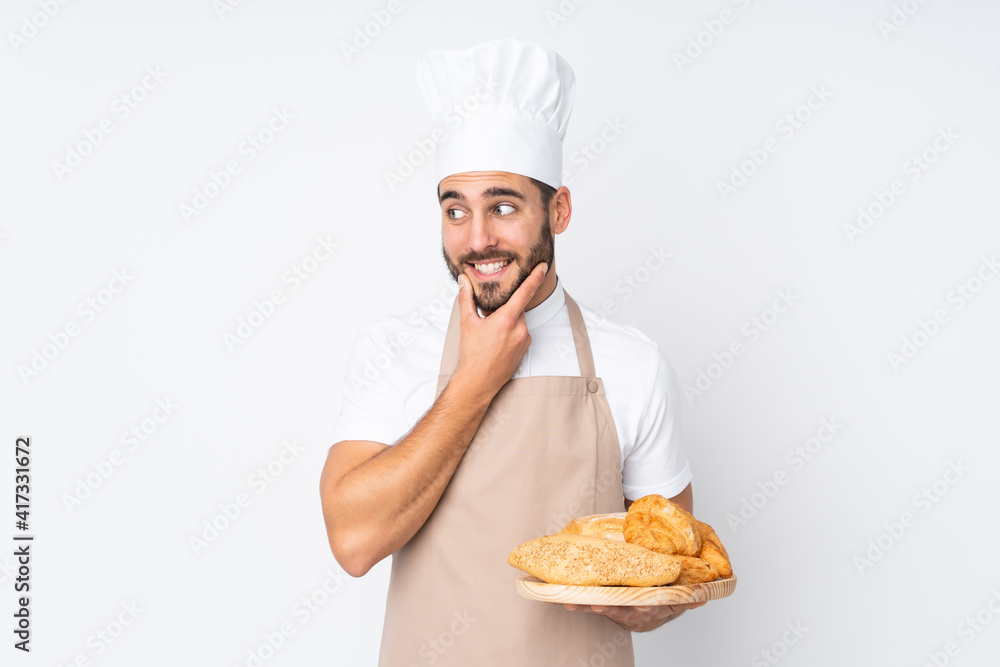 Male baker holding a table with several breads isolated on white background thinking an idea Male baker holding a table with several breads isolated on white background thinking an idea