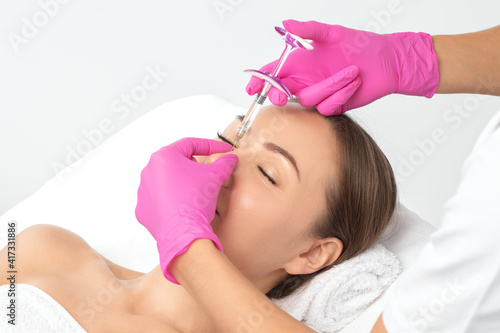 The doctor does injections to correct the hump on the nose with the beauty of the blonde. The beautician doees injections against wrinkles on the face. Women's cosmetology in a beauty salon.