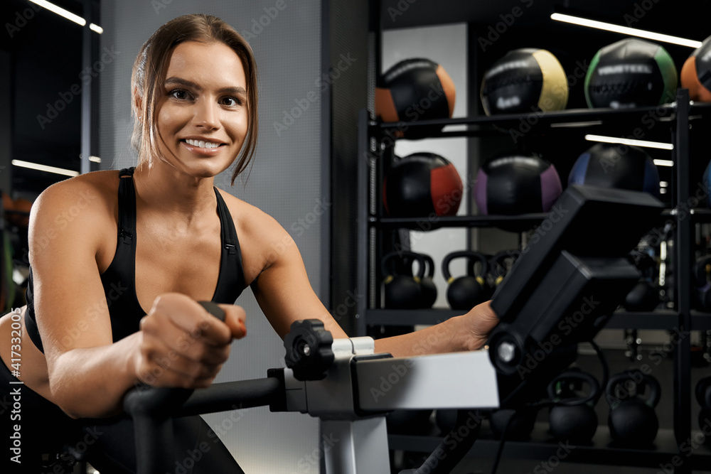 Fototapeta premium Smiling young woman engaged on exercise bike.