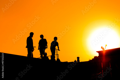Unrecognizable group of teenage boy silhouettes with scooters standing together against orange sunset sky at skatepark. Sport  extreme  freestyle  outdoor activity concept