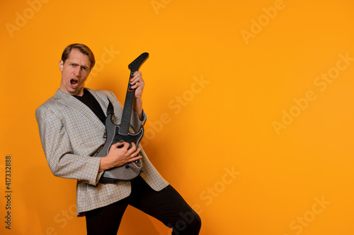 stylish and cool guy in a suit and with a game guitar on a yellow background, have fun and have a good time