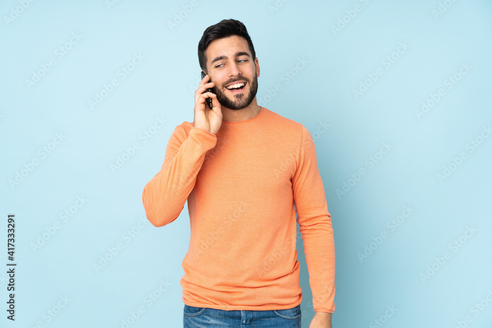 Caucasian handsome man keeping a conversation with the mobile phone over isolated blue background Caucasian handsome man keeping a conversation with the mobile phone over isolated blue background