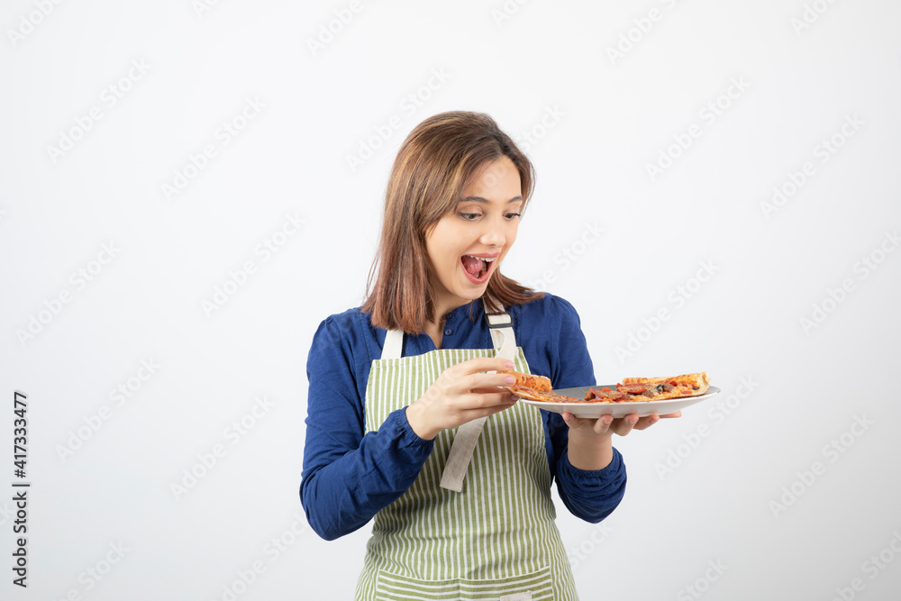 Portrait of young woman in apron looking at delicious pizza on white background Portrait of young woman in apron looking at delicious pizza on white background