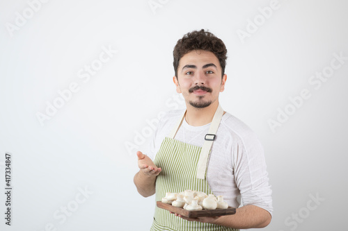 Portrait of male cook showing raw mushrooms on white background