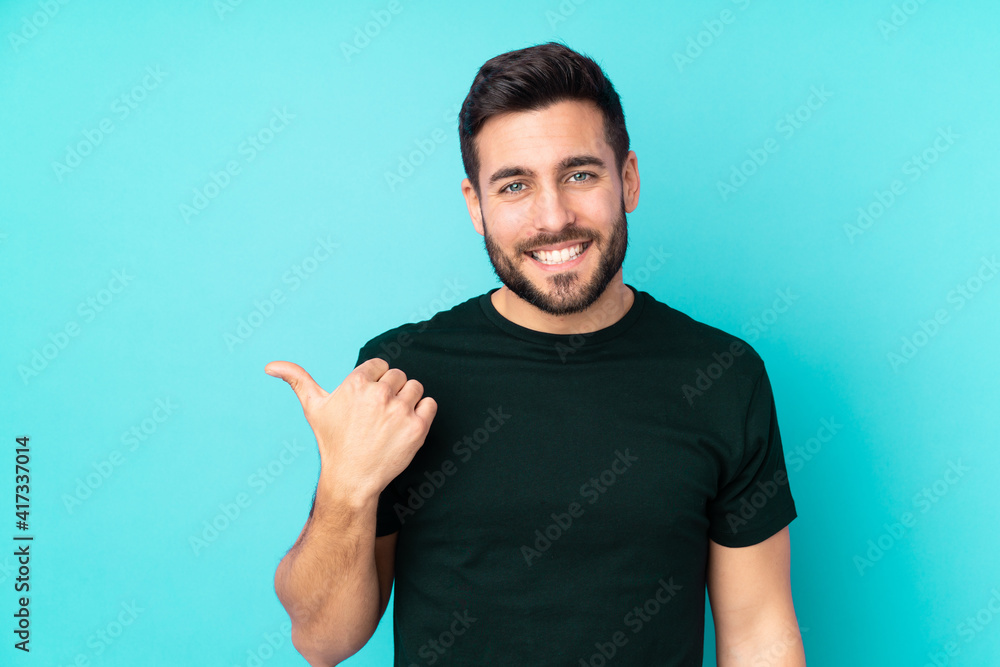 Fototapeta premium Caucasian handsome man isolated on blue background pointing to the side to present a product