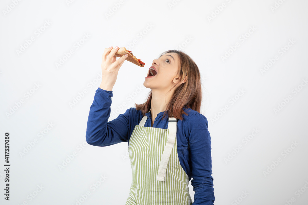 Portrait of woman in apron eating slice of pizza on white background Portrait of woman in apron eating slice of pizza on white background