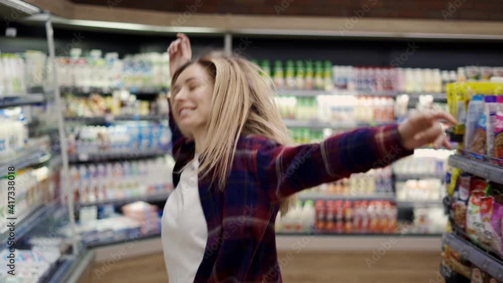 Happy young woman dances in supermarket, whirling, having fun Happy young woman dances in supermarket, whirling, having fun