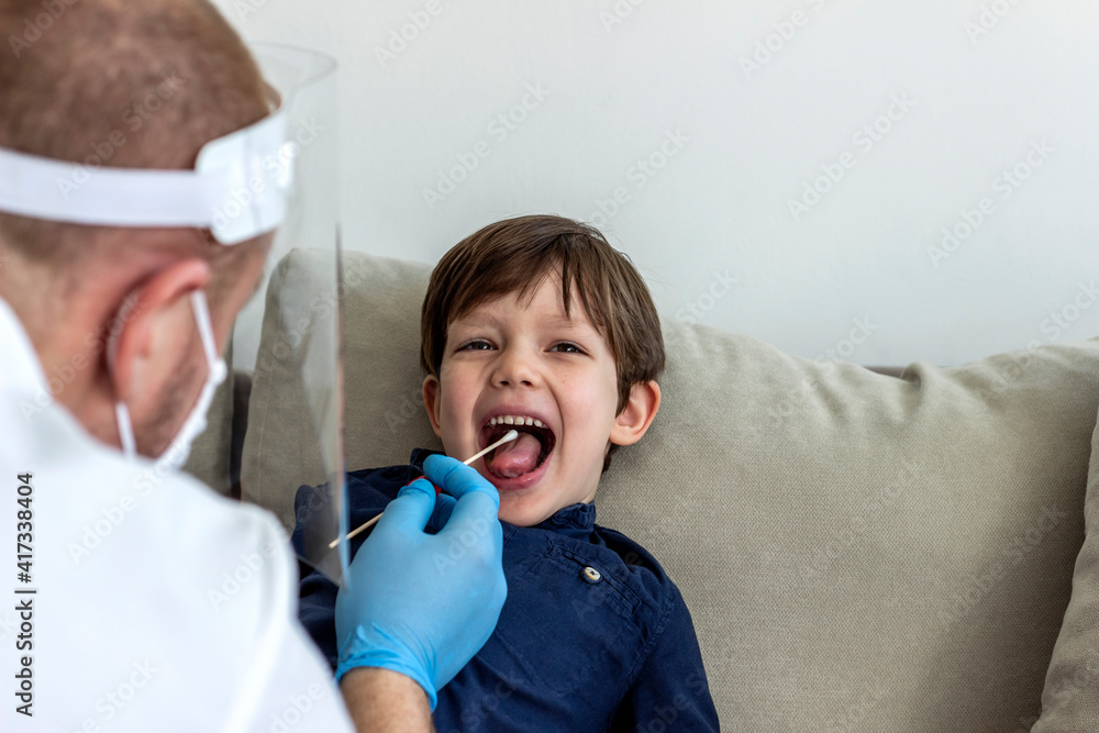 Caucasian boy having PCR test during coronavirus pandemic. Doctor takes a cotton swab test from child mouth to analyse for covid-19. Pediatrician using a swab to take a sample from a patient's throat. Caucasian boy having PCR test during coronavirus pandemic. Doctor takes a cotton swab test from child mouth to analyse for covid-19. Pediatrician using a swab to take a sample from a patient's throat.
