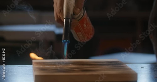 Craftsman carpenter scorches a wooden board with a gas-burner in slow motion, wood aging, scorched surface structure, woodworking at workshop with blowtorch, 4k 60p Prores 422 HQ 10 bit photo