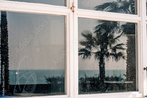 Reflection of sky  sea and palm trees in dirty window glass with white frame  309 