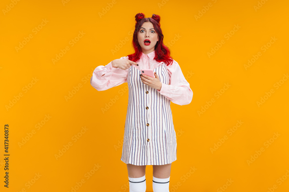 Shocked girl with red hair pointing finger at her mobile phone Shocked girl with red hair pointing finger at her mobile phone