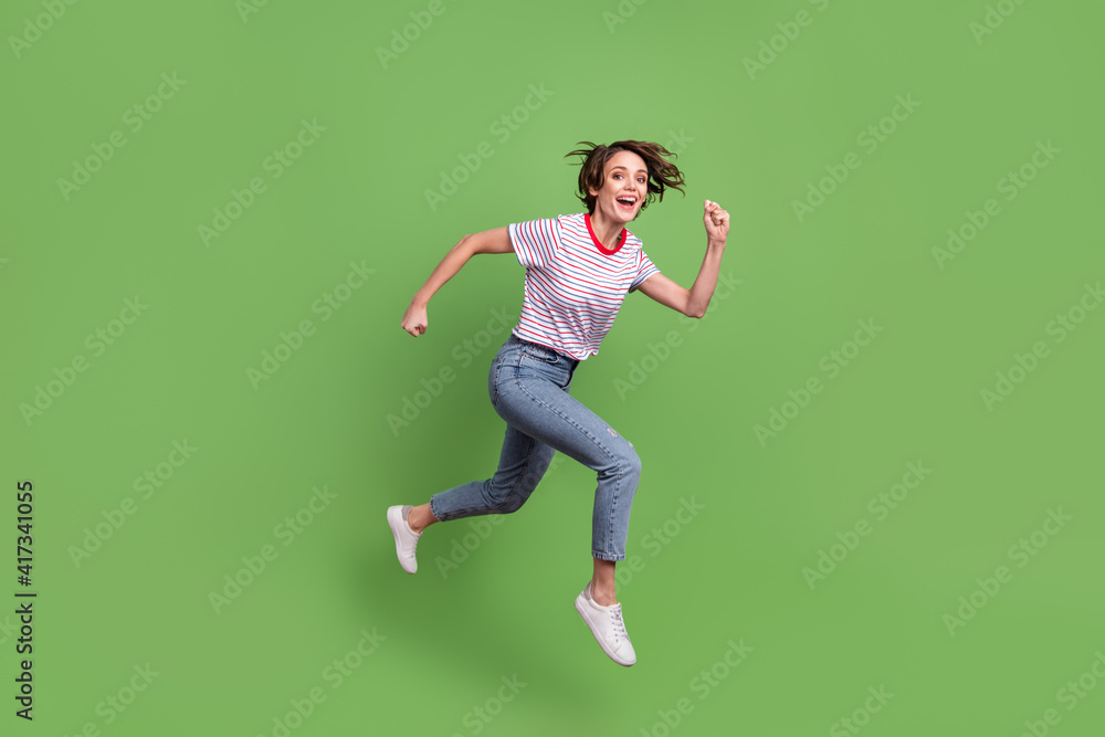 Full length body size profile side view of lovely cheerful girl jumping running action isolated over green pastel color background Full length body size profile side view of lovely cheerful girl jumping running action isolated over green pastel color background