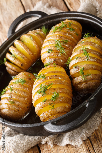 hasselback potatoes are thinly sliced potatoes that are baked to golden brown perfection with butter and garlic closeup in a pan on the table. Vertical