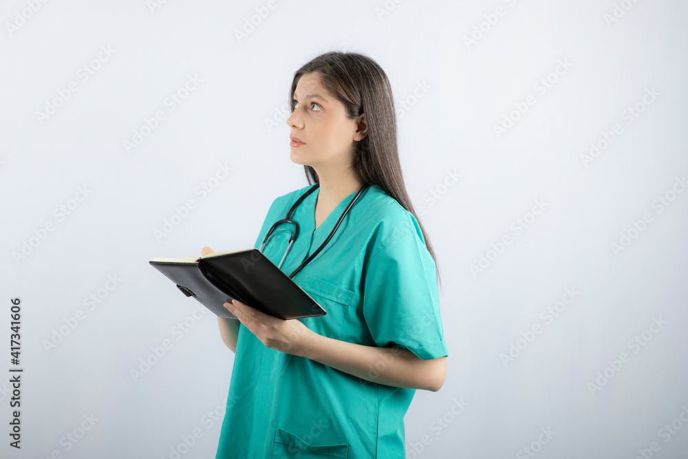 Photo of a young female doctor standing with notebook and pencil Photo of a young female doctor standing with notebook and pencil