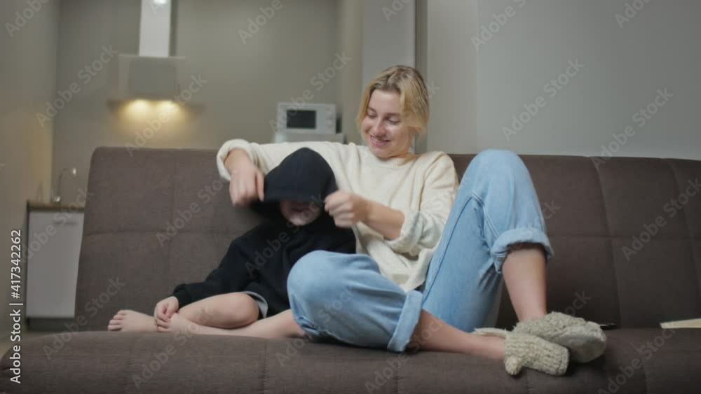 Young mother sits with her son on couch, watch TV and talks together Young mother sits with her son on couch, watch TV and talks together