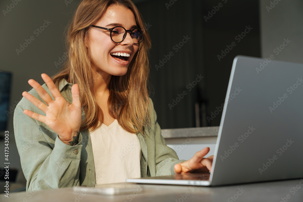 Happy nice woman waving hand and smiling while working with laptop Happy nice woman waving hand and smiling while working with laptop