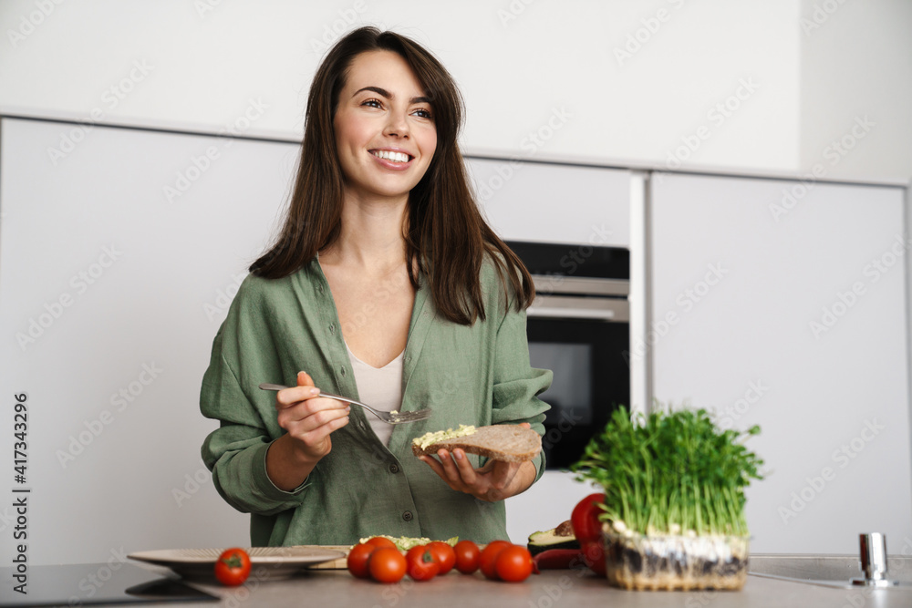 Joyful brunette woman smiling while preparing sandwich with avocado Joyful brunette woman smiling while preparing sandwich with avocado