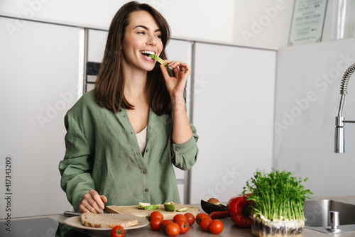 Joyful brunette woman tasting avocado while preparing sandwich