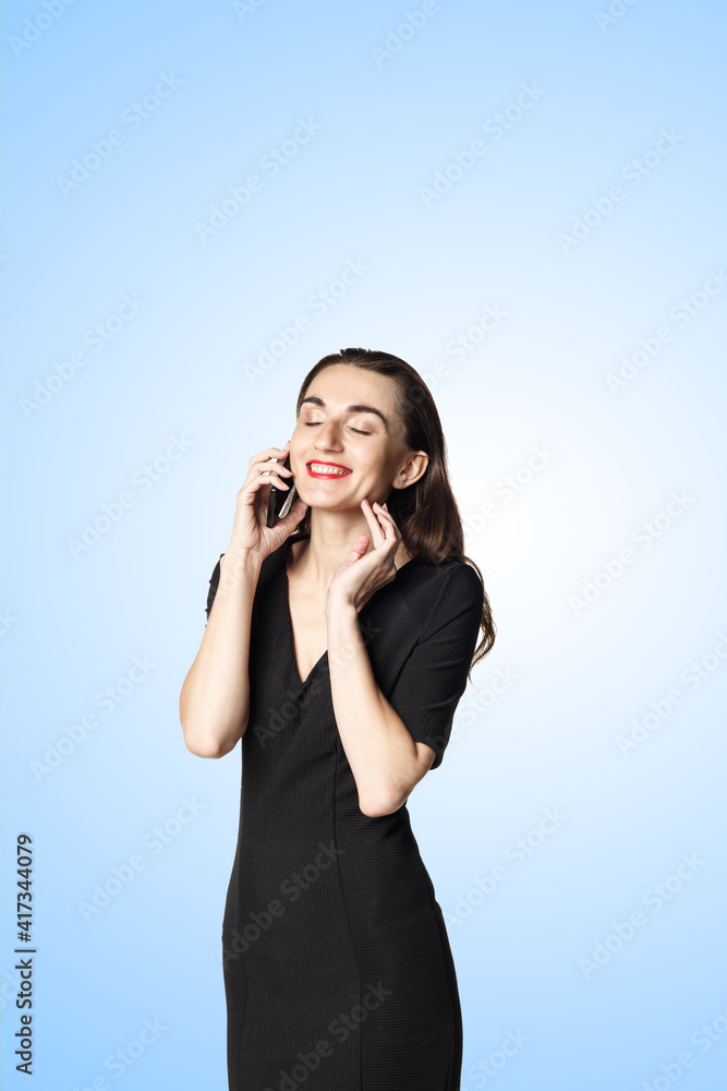 Business woman (fatal woman) in a black dress with red lipstick talking on the phone, isolated on a blue background Business woman (fatal woman) in a black dress with red lipstick talking on the phone, isolated on a blue background