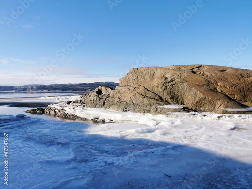 Cliff by a frozen lake in Hvittensand, Larvik during a sunny winter day photo