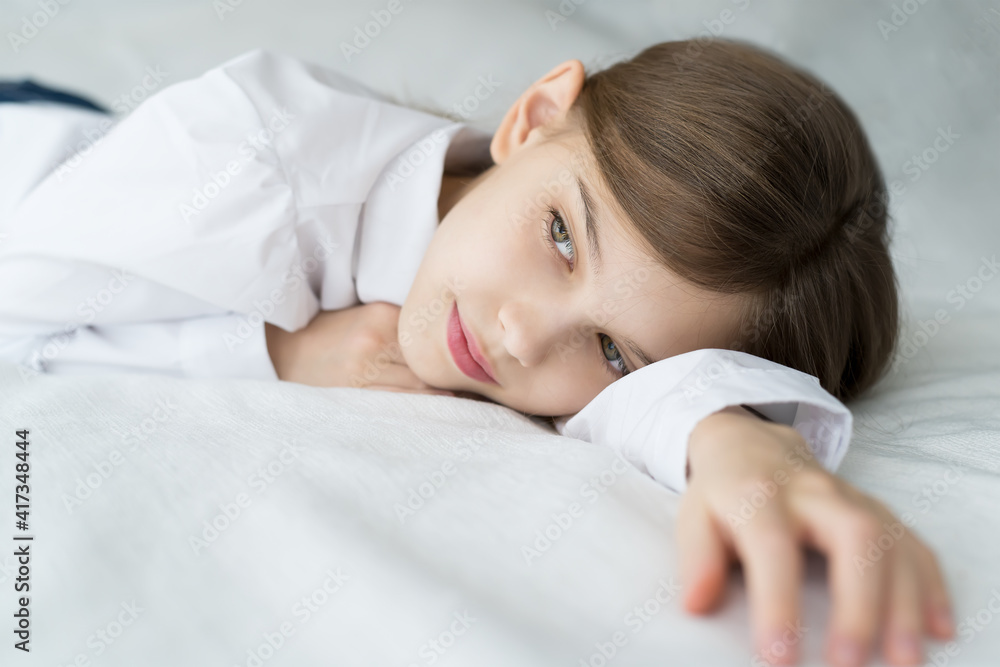 Close up shot of beautiful blonde caucasian little girl lying on a bed in a white shirt, looking calm and dreamy Close up shot of beautiful blonde caucasian little girl lying on a bed in a white shirt, looking calm and dreamy