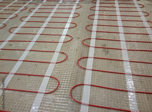 Closeup of concrete and red electrical wires. Electric floor heating system installation in new house. Closeup of concrete and red electrical wires