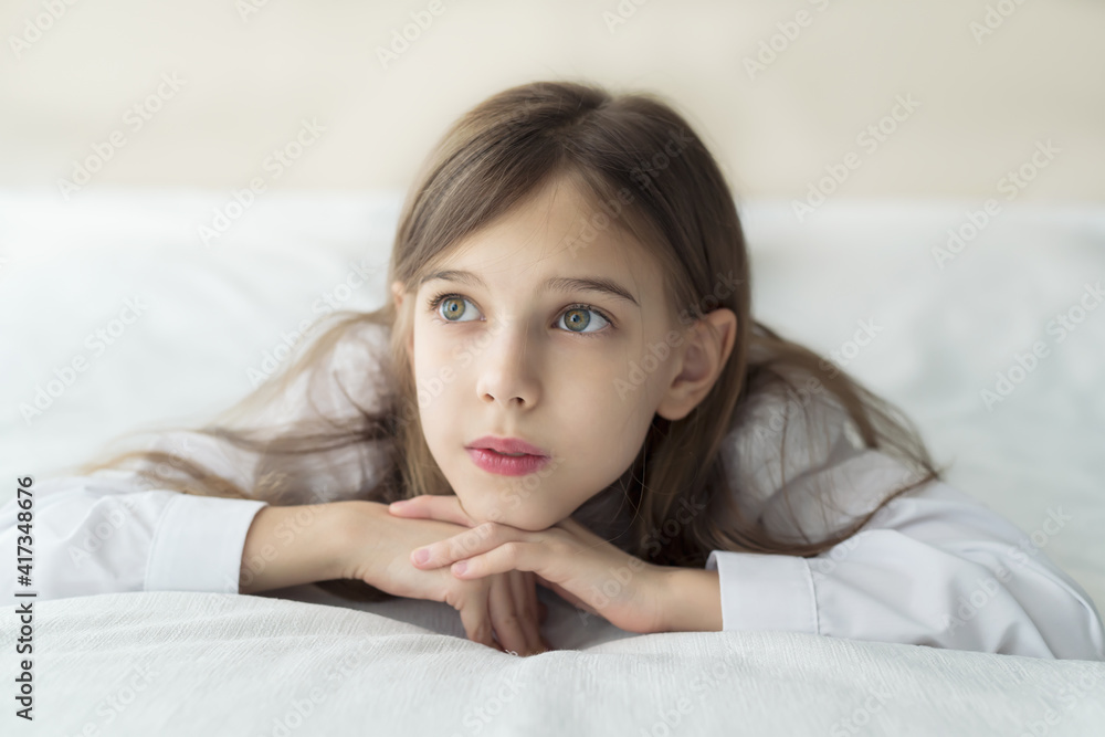 Close up shot of beautiful blonde caucasian little girl lying on a bed in a white shirt, looking calm and dreamy Close up shot of beautiful blonde caucasian little girl lying on a bed in a white shirt, looking calm and dreamy
