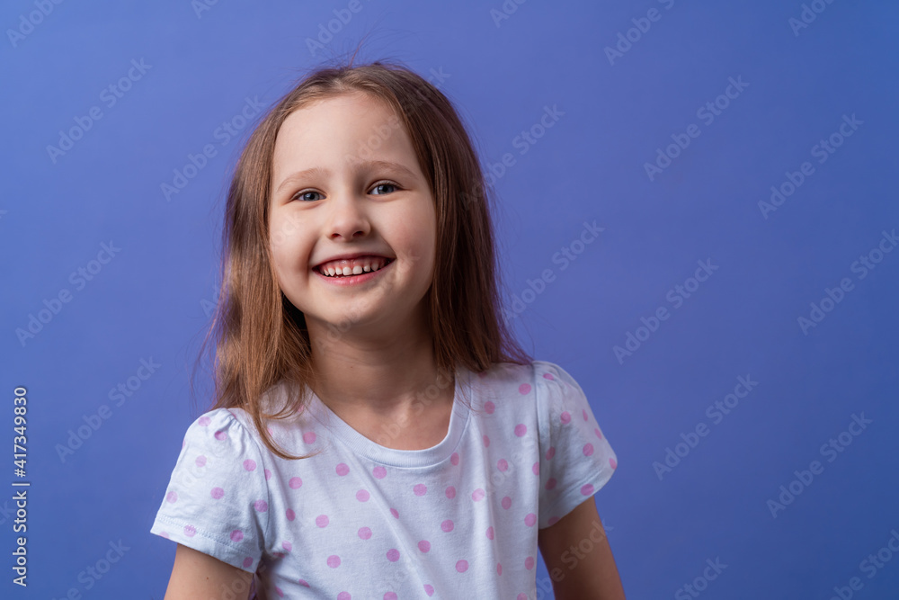 Little girl 5 years old with blonde hair in a T-shirt with colored polka dots standing happily smiling on purple background. Close-up. the model is having fun and feels overwhelmed, amazed. Little girl 5 years old with blonde hair in a T-shirt with colored polka dots standing happily smiling on purple background. Close-up. the model is having fun and feels overwhelmed, amazed.