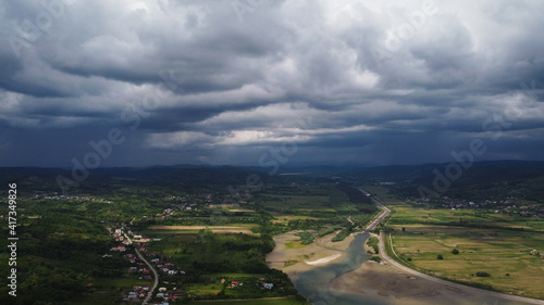 Photos Aerial shot of houses on a greenfield near a river under a gloomy sky