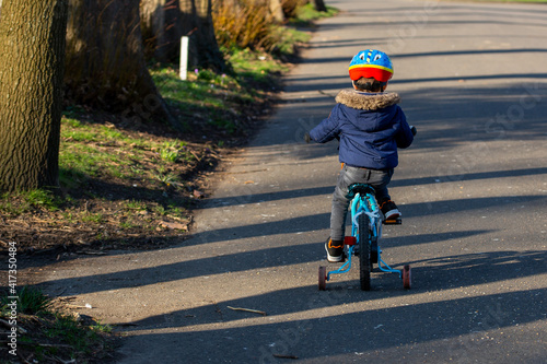 A small boy wearing a cycle helmet riding a bike in the park with stabilisers or stabilizers