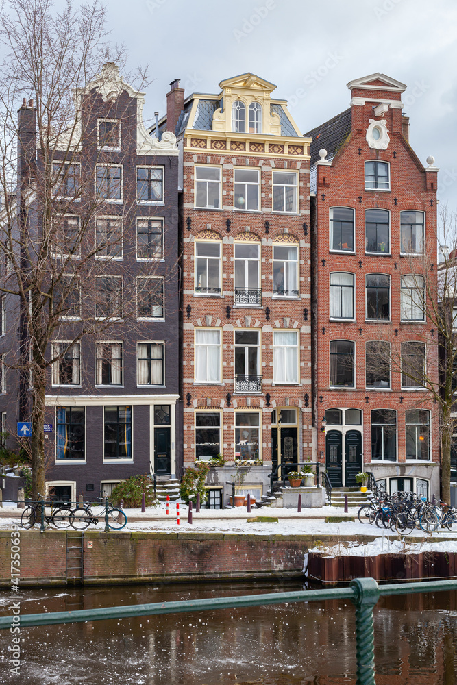 A winter scene of Amsterdam canal houses in the snow with ice on the water, vertical