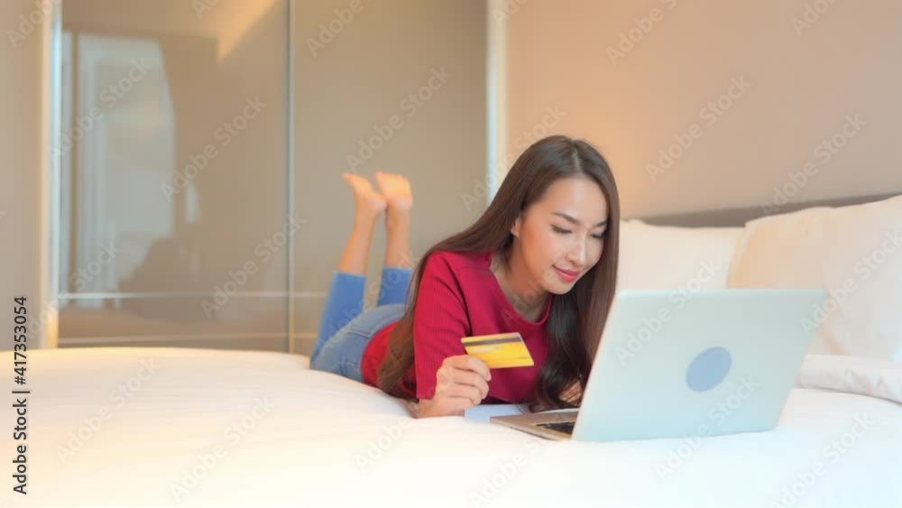 A young asian woman shopping online using credit card and laptop computer in bed of family home A young asian woman shopping online using credit card and laptop computer in bed of family home