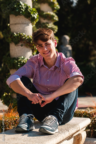 chico guapo joven caucásico con camisa de rayas rojas sentado en un banco en el parque del retiro de Madrid (Vida sana - Deporte)