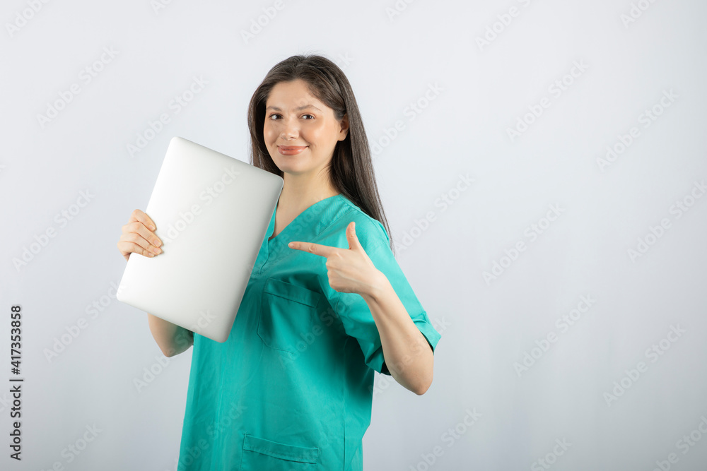 Fototapeta premium Photo of young nurse pointing at laptop on white background