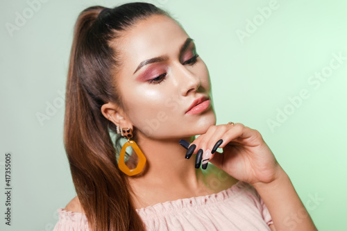 Beautiful girl with evening green makeup on green background. Eye make-up and sensual lips. Elegant hairstyle. Brunette with tassel  bijouterie earrings. High fashion.